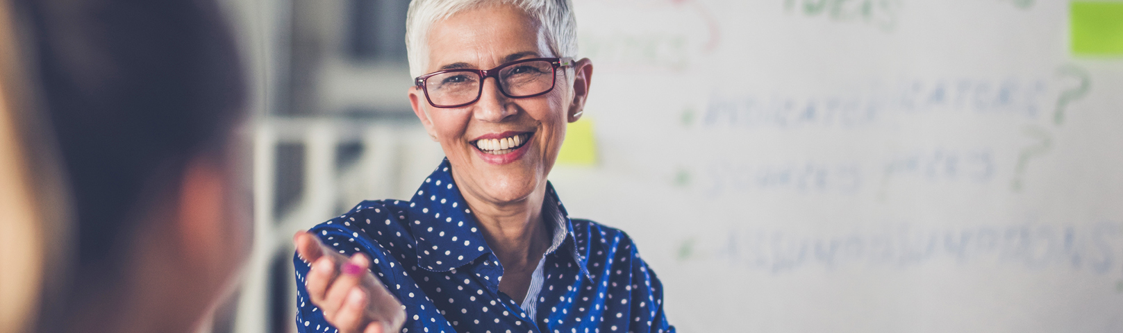 a mature business woman smiles while speaking to her diverse team in front of a whiteboard